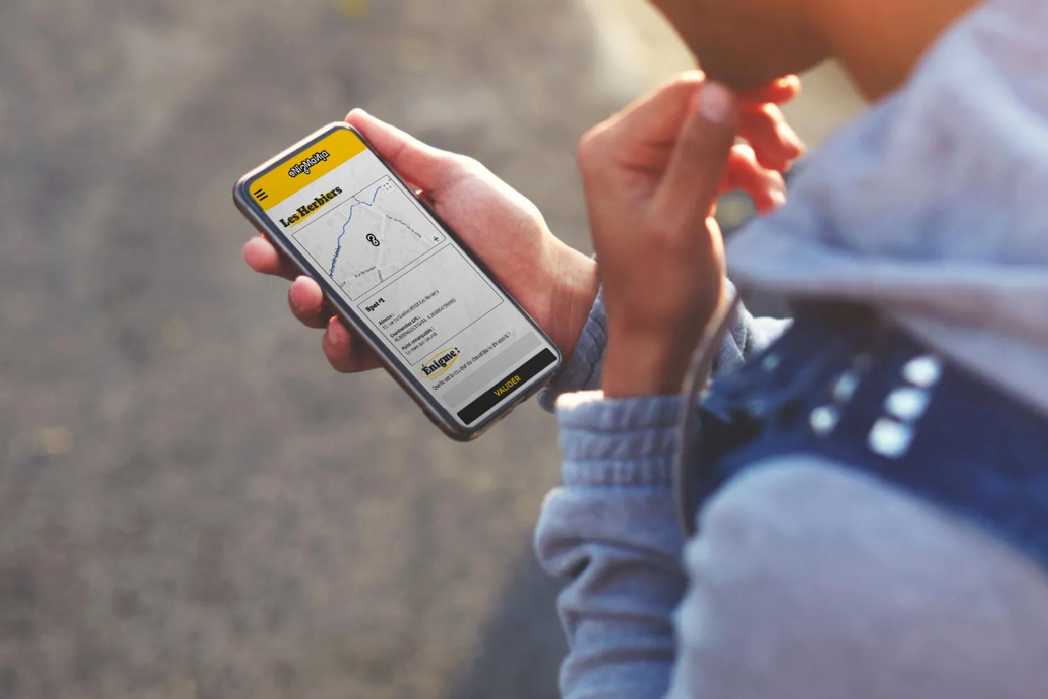 Main tenant un smartphone affichant l'interface du parcours Enigmania