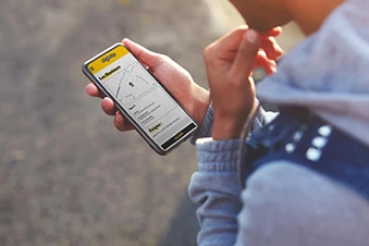 Main tenant un smartphone affichant l'interface du parcours Enigmania, jeux de piste entre amis en Vendée